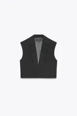 Chaleco corto de Zara con cuello solapa, diseño sin mangas con hombreras y forro interior. Presenta un corte estructurado con cierre frontal mediante botón oculto.