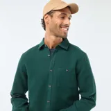 Camisa de manga larga de tejido gofrado en color verde oscuro, con cuello clásico, cierre frontal de botones y un bolsillo aplicado en el pecho.