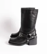 Bota de cuero negra con caña media, punta cuadrada, taco bloque y arnés con hebillas y tachas plateadas.