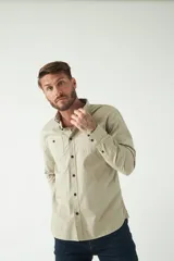 Camisa de hombre color beige con efecto stone wash, corte regular, cuello clásico, cierre frontal con botones, dos bolsillos con solapa abotonada en el pecho y mangas largas con puños abotonados.