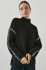 Sweater negro de punto con cuello alto y bordados blancos en sisas y mangas.