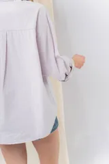 Camisa verde pastel de algodón, corte oversize, con cuello camisero, cierre con botones, mangas largas con puños con volados de encaje blanco, dos bolsillos frontales con solapa y ruedo irregular. 