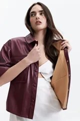 Camisa de manga corta confeccionada en cuero sintético color bordó, con cuello clásico, cierre frontal de botones metálicos y dos bolsillos frontales con solapa.