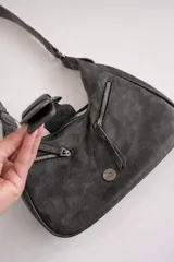 Cartera de hombro de tamaño compacto con acabado texturizado efecto cuero desgastado. Presenta un diseño con cierre superior, bolsillos frontales con cierre y una solapa central decorativa con hebilla metálica. Incluye asa fija para llevar al hombro.