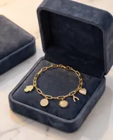 Pulsera de cadena de eslabones dorada con cinco dijes colgantes decorados con circonias: un corazón, una mano de Hamsa, un sol, un hueso de la suerte y un círculo.