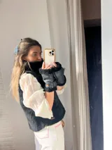 Chaleco negro de cuero con interior de piel sintética, cuello alto y cierre frontal con cremallera.