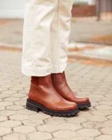 Botas cortas de cuero color marrón con suela track negra de goma. Presentan un diseño de corte clásico con paneles laterales texturizados y cierre lateral interno.