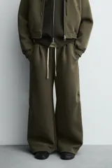 Pantalón de corte wide fit confeccionado en tejido técnico compacto con efecto neopreno. Presenta cintura elástica con cordón ajustable, pliegues frontales, bolsillos laterales y detalle de pliegues en las rodillas con aplicaciones metálicas.