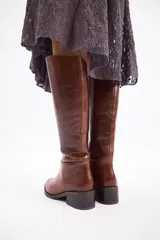 Bota de caña alta confeccionada en cuero vacuno, con taco cuadrado bajo y punta redondeada.