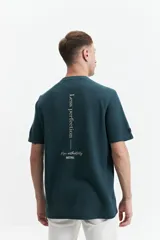 Remera de manga corta, color verde oscuro, con textura tipo waffle o piqué. Presenta un estampado vertical en la espalda con texto en blanco.