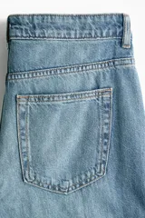 Jean de tiro alto y corte baggy, confeccionado en denim de algodón rígido en color celeste con efecto deslavado. Presenta diseño de cinco bolsillos, piernas rectas y holgadas, y cierre frontal con botón y cremallera.