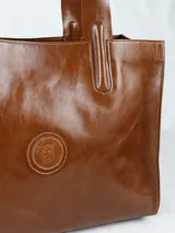 Cartera de cuero color marrón con compartimiento interno removible y logo circular en el frente.