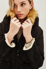 Campera negra de diseño híbrido con cuerpo acolchado en forma de rombos y mangas de textura lisa. Presenta un cuello de piel sintética desmontable en tono marrón y detalles de corderito en los puños y el ruedo. Incluye cierre frontal y cordones ajustables en la cintura.