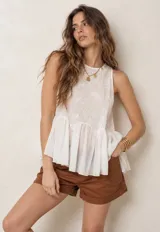 Blusa sin mangas de color blanco, confeccionada en tejido semitransparente con detalles bordados en el pecho y diseño de volados en la parte inferior.