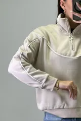 Buzo deportivo color beige con cuello alto y cierre frontal parcial. Presenta costuras decorativas con ribetes blancos en el pecho y a lo largo de las mangas. Posee puños y ruedo elásticos.
