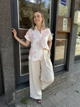 Camisa blanca de manga corta con cuello clásico y cierre frontal de botones, destacada por grandes bordados florales en tonos rosados.