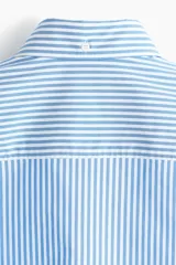 Camisa de corte relajado confeccionada en tejido de algodón con estampado de rayas verticales. Presenta cuello americano, cierre frontal con botones, un bolsillo en el pecho y mangas largas con puños abotonados.