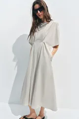 Vestido midi de popelín de algodón en color beige, con cuello redondo, manga corta y pliegues en la cintura. Presenta una falda en línea evasé y cierre en la espalda con cremallera oculta.