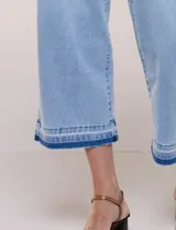 Jean cropped de denim celeste, con tiro alto, pernera ancha y recta, y diseño de cinco bolsillos. Presenta un dobladillo bicolor con flecos en tono más oscuro.