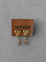 Aros colgantes con diseño de pieza superior en forma de pétalo color beige con borde metálico y dije inferior compuesto por tres cuentas de cristal facetado en tono ámbar.