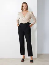 Enterito combinado de fiesta marca Julia Jordan. El torso es de lentejuelas color beige con escote en V cruzado y mangas largas abullonadas. La cintura es elastizada con lazo de ajuste y el pantalón es negro con bolsillos verticales. La espalda tiene cierre invisible y el torso está forrado.