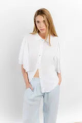 Camisa de lino color tostado, con cuello camisero y cierre frontal de botones. Se caracteriza por sus mangas cortas amplias y voluminosas que aportan un diseño fresco y liviano.