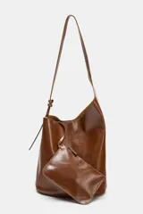 Bolso tipo saca de diseño asimétrico confeccionado en piel de color marrón. Cuenta con un asa de hombro ajustable y cierre mediante imán. Incluye una cartera con bolsillo extraíble en su interior.