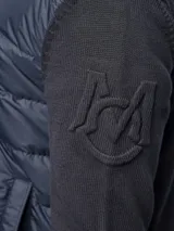 Campera híbrida Moncler con frente acolchado en color azul marino y mangas de tejido de punto en color negro. Presenta cuello alto tejido, cierre frontal completo y bolsillos laterales con cierre. Incluye el logo de la marca en el pecho y en la manga.
