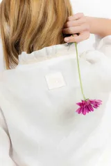 Blusa corta blanca de lino con mangas 3/4 abullonadas, escote en V con volados y cierre con lazos.