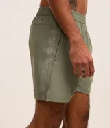 Bermuda deportiva masculina color verde oliva, confeccionada en poliéster y elastano. Posee cintura elástica con cordón interno ajustable y estampa reflectante en el lateral. Ideal para actividades deportivas.