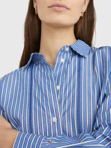 Camisa de manga larga a rayas verticales azules y blancas, con cuello inglés y corte amplio. Presenta detalles distintivos de la marca Tommy Hilfiger y logo bordado en el puño.