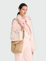 Cartera tipo bucket en tamaño XS, confeccionada en rafia natural con detalles en cuero color tostado. Presenta un cierre de cordón ajustable con el icónico detalle de bambú metálico de la línea Le Roseau y una correa larga ajustable para llevar al hombro o cruzada.