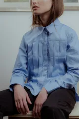 Camisa celeste de poplin de algodón, corte irregular con tablas al frente, cuello clásico y mangas largas.