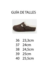 Zueco de gamuza sintética color kaki con forro interno de corderito sintético, tira ajustable con hebilla metálica y suela plana.