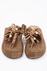 Zueco de cuero vacuno color marrón, con diseño de puntera reforzada y cordones decorativos con cuentas de madera en el empeine.