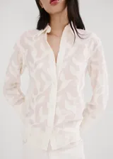 Blusa de diseño recto color crudo con diseño bordado floral, cuello camisero, manga larga con puños anchos abotonados y cierre delantero con botones.