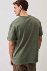 Remera de calce relajado y cuello redondo, color verde musgo con efecto lavado, y pequeño bordado de un morrón en el pecho.