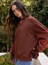 Buzo blanco de jogging sin friza, con cuello redondo y bordado floral marrón en las mangas.