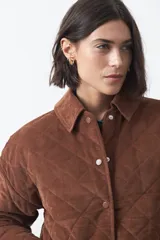 Campera capitoneada de algodón con diseño matelaseado, cuello camisero y cierre frontal con botones a presión. Presenta un corte relajado y bolsillos frontales.