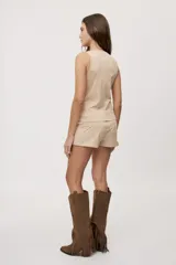 Short de tiro bajo con textura efecto gamuza color beige, bolsillos delanteros y detalle de cordones entrecruzados en la parte frontal.