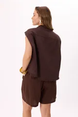Chaleco estilo cargo color marrón, con cuello camisero, cierre frontal de botones negros y dos bolsillos frontales con solapa. Presenta detalles de terminaciones desflecadas en el ruedo y en los bolsillos.