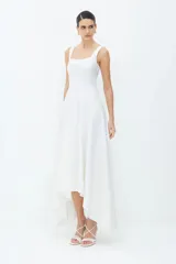 Vestido midi de algodón compacto, de color blanco, con corte entallado en el torso y falda amplia de corte asimétrico, más corta adelante y larga atrás. Presenta escote cuadrado y tirantes anchos.