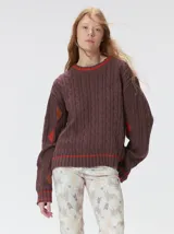 Sweater de punto con diseño de ochos en color verde, cuello redondo con detalle de franja en contraste, y apliques de rombos en las mangas. Presenta un bordado con la letra M en el pecho.