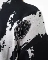 Buzo de punto con diseño abstracto en blanco y negro, con estampado gráfico estilo gótico en el pecho y detalles de roturas desgastadas en el tejido.