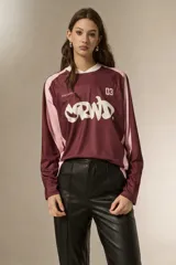 Remera de manga larga estilo deportivo, confeccionada en tejido técnico. Presenta un diseño color block en tonos bordó y rosa, con cuello mao y estampado gráfico frontal en color blanco.