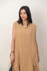 Vestido midi de lino color beige, sin mangas y con cuello redondo. Cuenta con un diseño irregular con detalle de volado vertical a un costado.