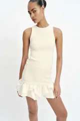 Vestido corto de color blanco con cuello redondo y diseño sin mangas. Presenta un cuerpo de tejido bouclé texturizado y un bajo acabado con volantes de tejido ligero.