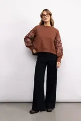 Buzo de cuello redondo con mangas largas, confeccionado en tejido de algodón con spandex. Presenta un diseño liso en el cuerpo y mangas con bordado floral de gran tamaño en contraste.