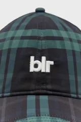 Gorra estilo béisbol de seis paneles con visera curva, confeccionada en tejido con estampado a cuadros en tonos verde oscuro y negro. Cuenta con el logo de la marca bordado en color blanco en el frente y cierre ajustable en la parte trasera.