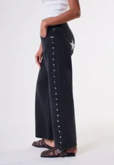 Jean de corte recto y tiro bajo, color negro, con diseño de estrellas blancas estampadas en los bolsillos traseros y detalles de tachas metálicas en los laterales.